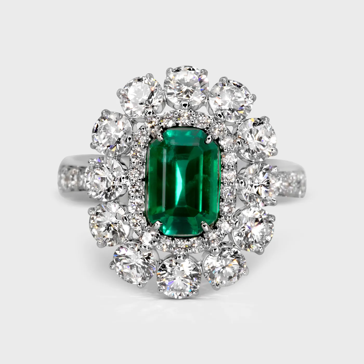 Monaco white gold ring by ValeOro with a rectangular green emerald framed by a diamond halo and round diamonds, front view