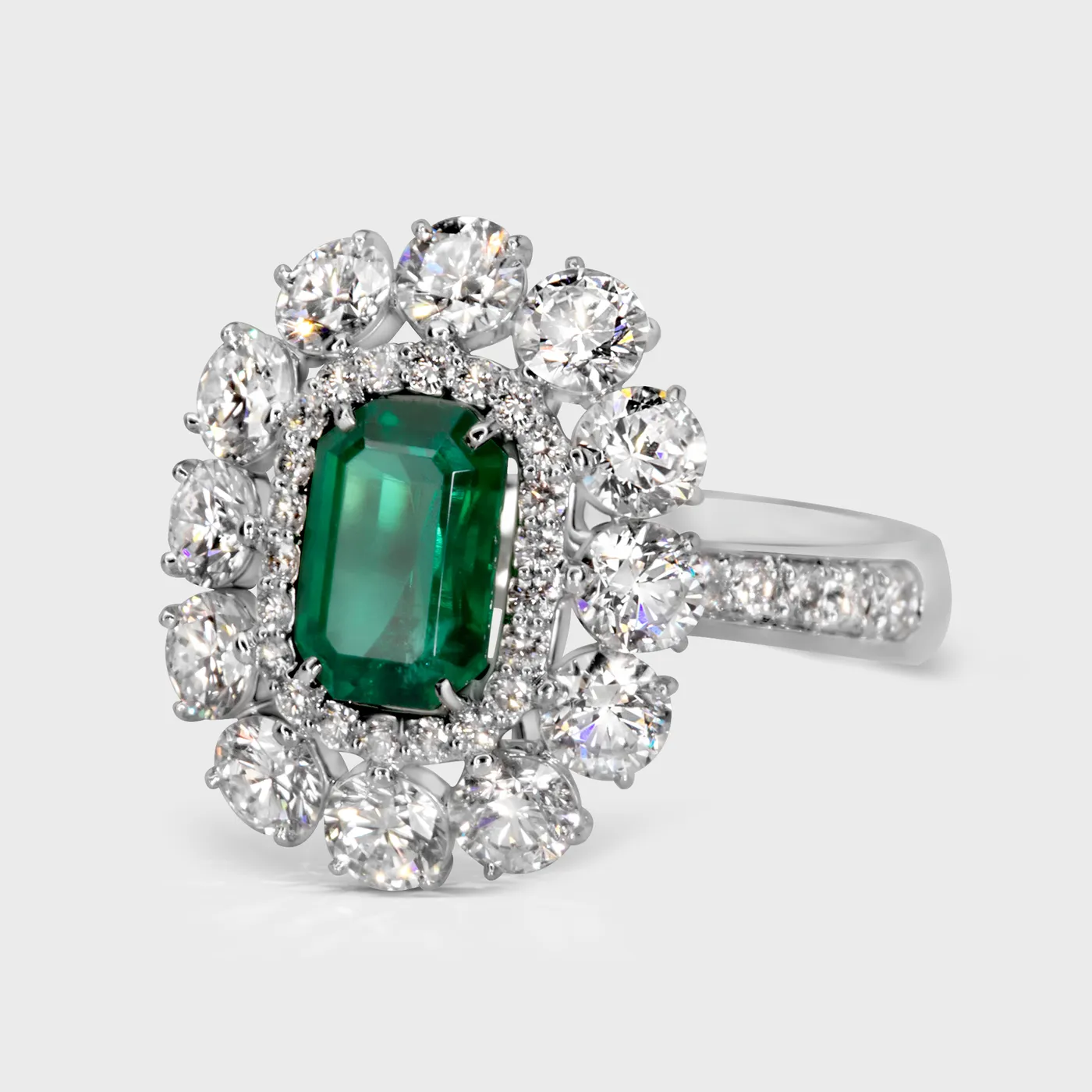 Monaco white gold ring by ValeOro with a green emerald in a symmetrical cluster of round diamonds, three-quarter view