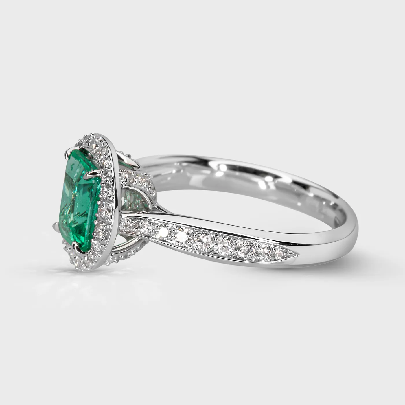 Ural white gold ring by ValeOro with a green emerald and diamond halo on a pavé-set band, three-quarter view