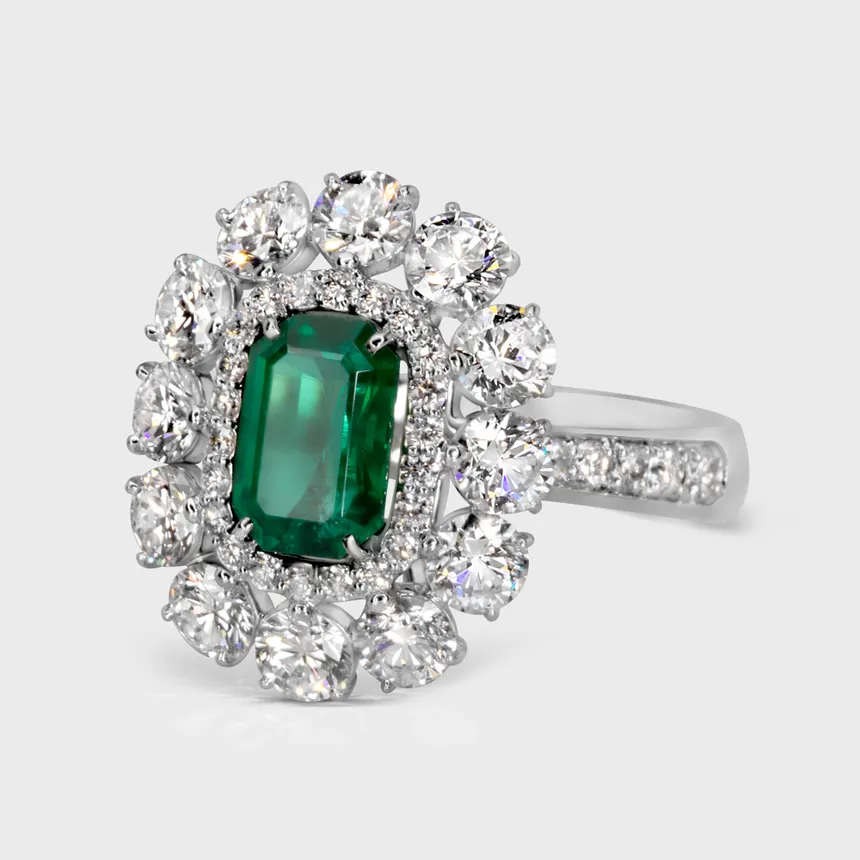 Monaco white gold ring by ValeOro with a green emerald in a symmetrical cluster of round diamonds, three-quarter view