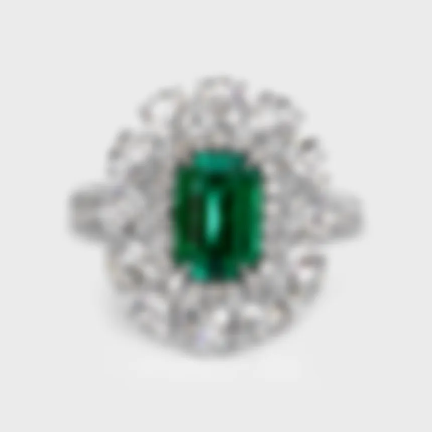 Monaco white gold ring by ValeOro with a rectangular green emerald framed by a diamond halo and round diamonds, front view
